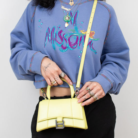 Person wearing a blue sweatshirt with colorful text and holding a yellow handbag against a white background