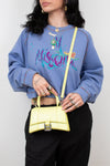 Person wearing a blue sweatshirt with colorful text and holding a yellow handbag against a white background