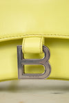 Close-up of a yellow handbag with a silver 'B' logo on a light background