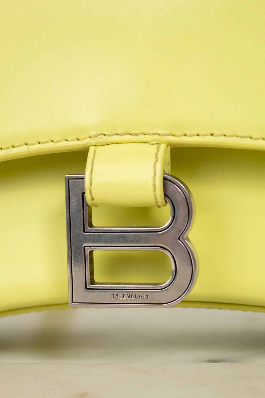 Close-up of a yellow handbag with a silver 'B' logo on a light background