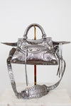 Silver handbag with intricate designs on a white background