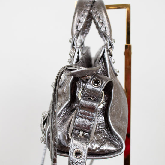 Side view of silver handbag with detailed straps on purse stand with a white background