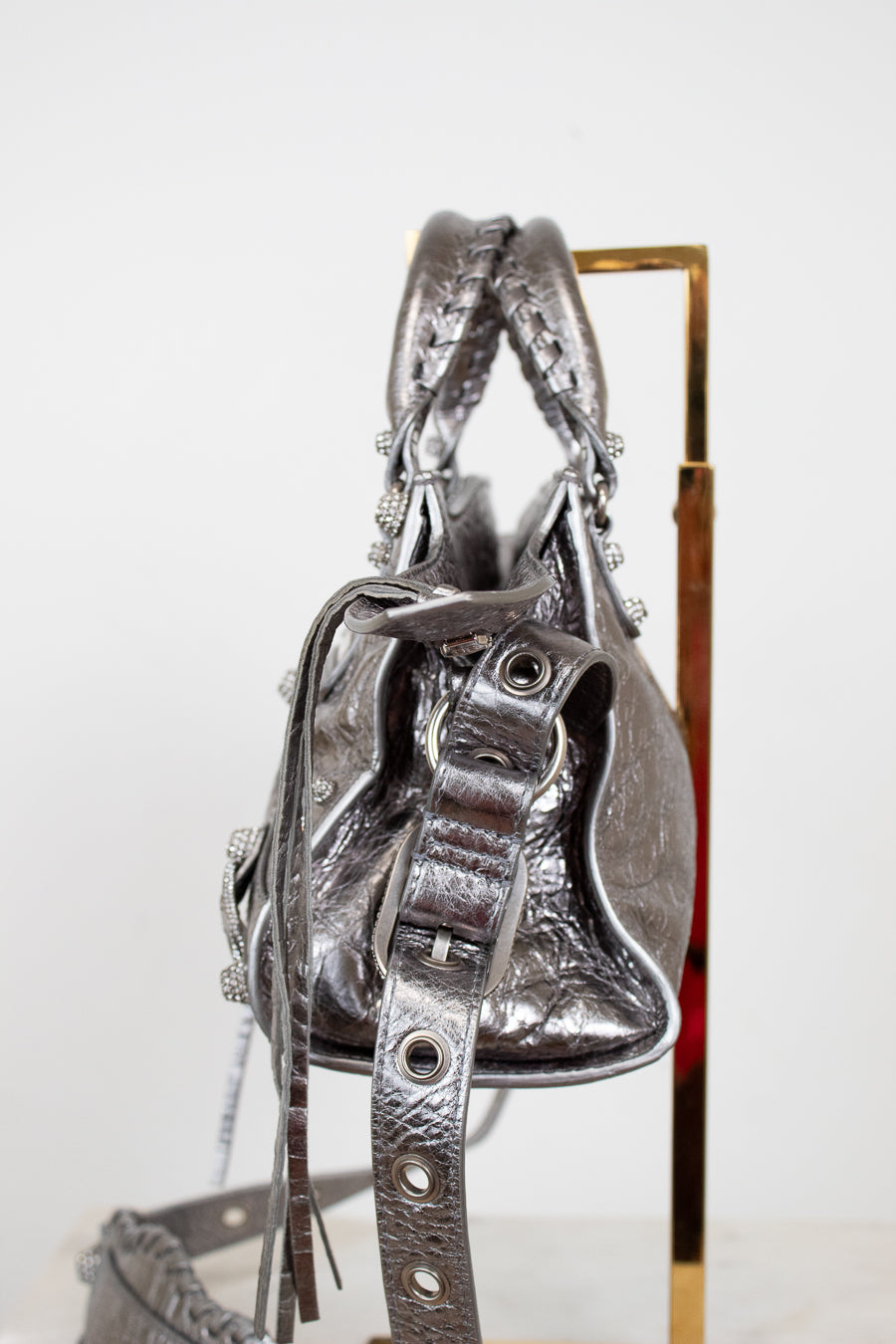 Side view of silver handbag with detailed straps on purse stand with a white background