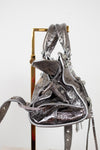 Side view of silver metallic handbag with decorative elements on a stand against a white background