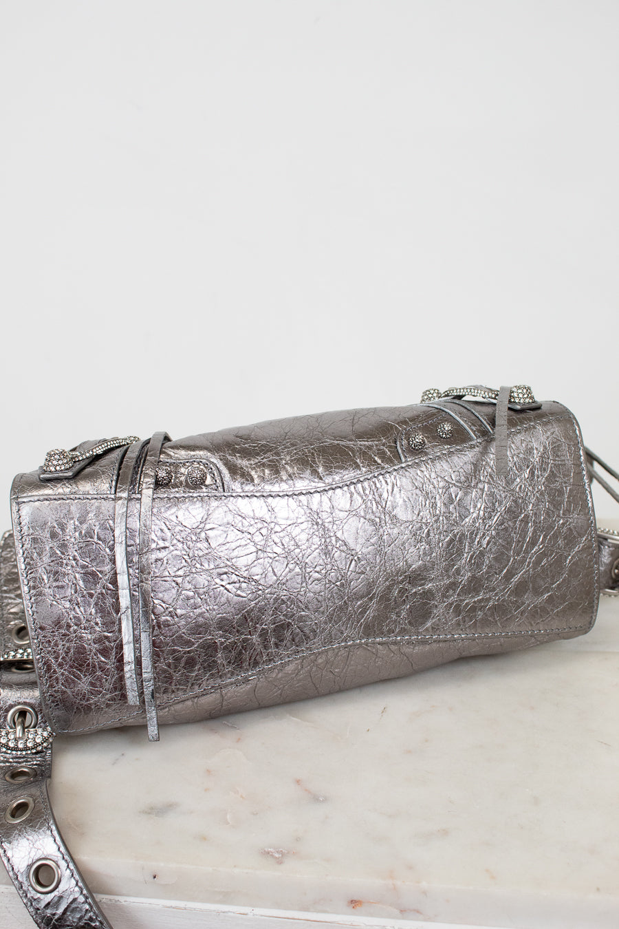 Bottom of silver crinkle metallic handbag with  on a white surface