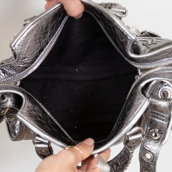 Top view of silver handbag with intricate designs held open by a person's hands.