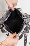 Top view of silver handbag with intricate designs held open by a person's hands.