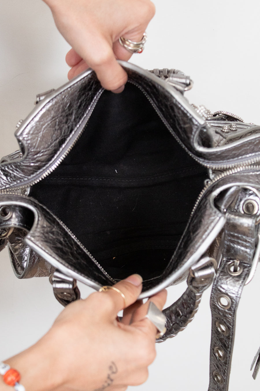 Top view of silver handbag with intricate designs held open by a person's hands.