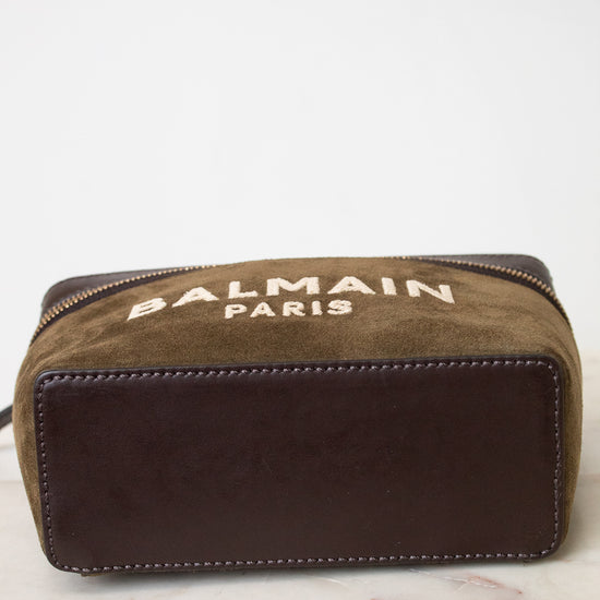 A Balmain Paris zippered pouch in brown suede and dark brown leather, resting on a white marble surface against a white background.