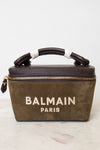 A Balmain Paris handbag in olive green suede with dark brown leather trim and handle, featuring gold hardware and white embroidered branding on the front, set against a light background.