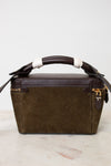 A structured rectangular handbag in dark brown leather and olive green suede, featuring a wrapped bamboo handle and gold-tone hardware, set against a clean off-white background.