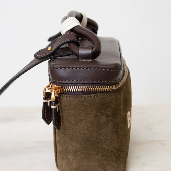 A small structured handbag in dark brown leather and olive green suede, featuring a top zipper with gold-tone hardware and a dark brown rope handle, set against a plain white background.