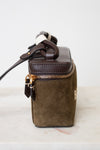 A small structured handbag in dark brown leather and olive green suede, featuring a top zipper with gold-tone hardware and a dark brown rope handle, set against a plain white background.