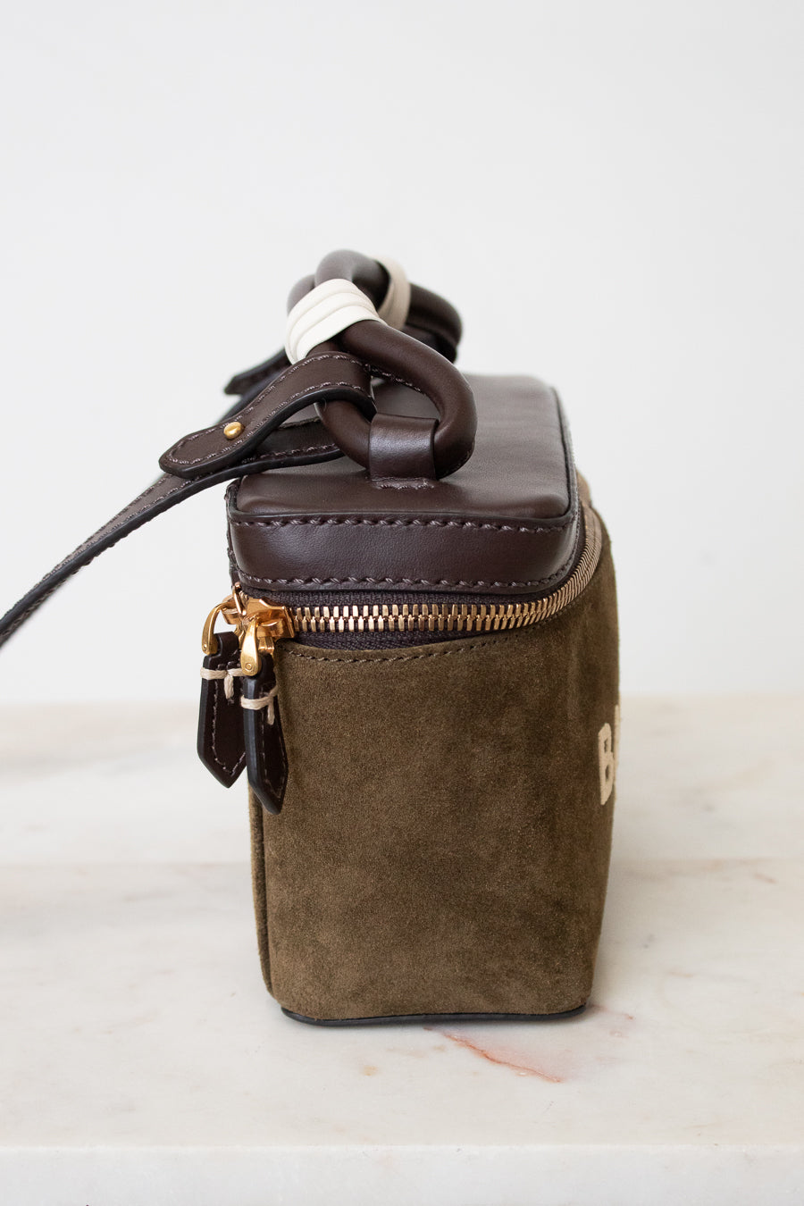 A small structured handbag in dark brown leather and olive green suede, featuring a top zipper with gold-tone hardware and a dark brown rope handle, set against a plain white background.