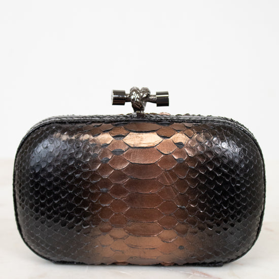 Black and bronze snakeskin patterned clutch bag on a white background