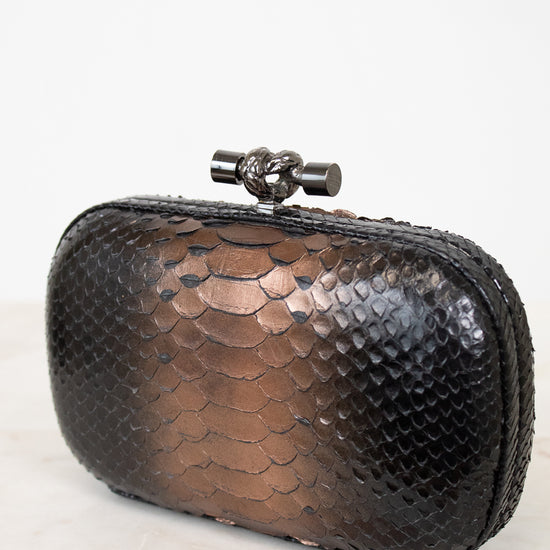 Black metallic clutch bag with a decorative clasp on a white background