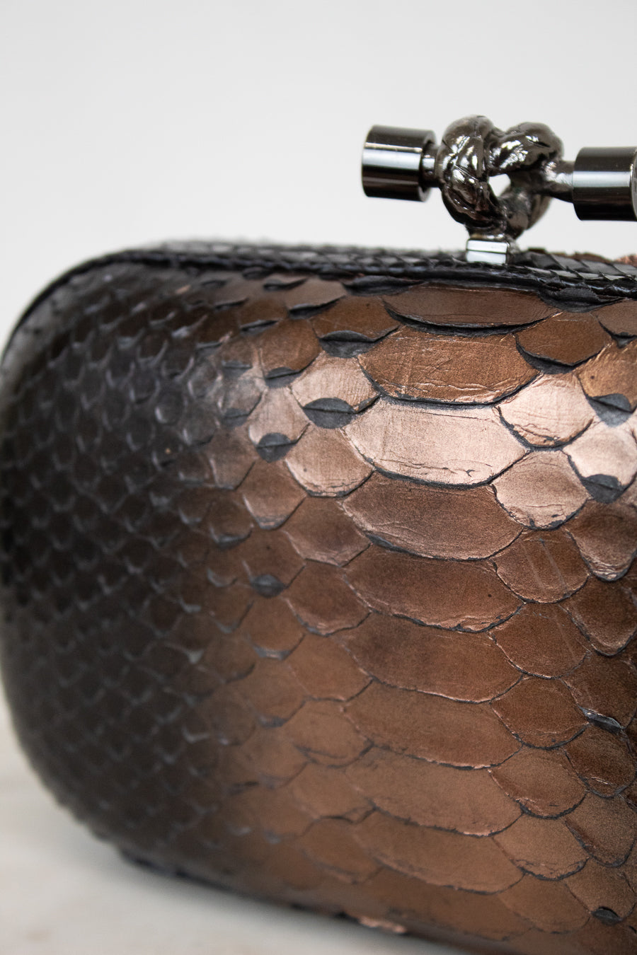 Close-up of a brown textured clutch bag with a metallic clasp on a light background