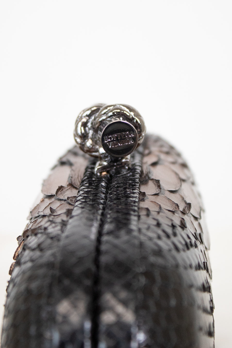 Close-up of a black clutch with a brand logo on a white background