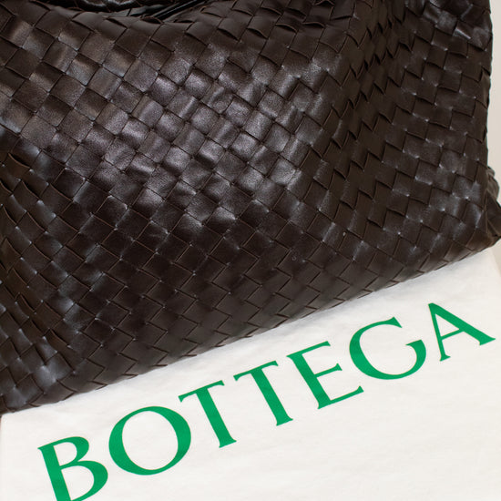 Brown woven oversized tote on a white surface with 'Bottega' dust bag.