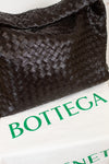 Brown woven oversized tote on a white surface with 'Bottega' dust bag.