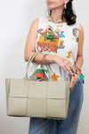 Person holding a light green woven handbag wearing a colorful sleeveless shirt with graphic designs.