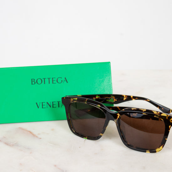 Sunglasses with tortoiseshell frame and brown lenses on a marble surface with a green Bottega Veneta box.