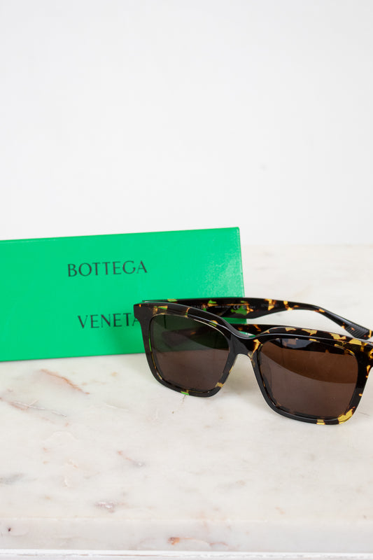 Sunglasses with tortoiseshell frame and brown lenses on a marble surface with a green Bottega Veneta box.