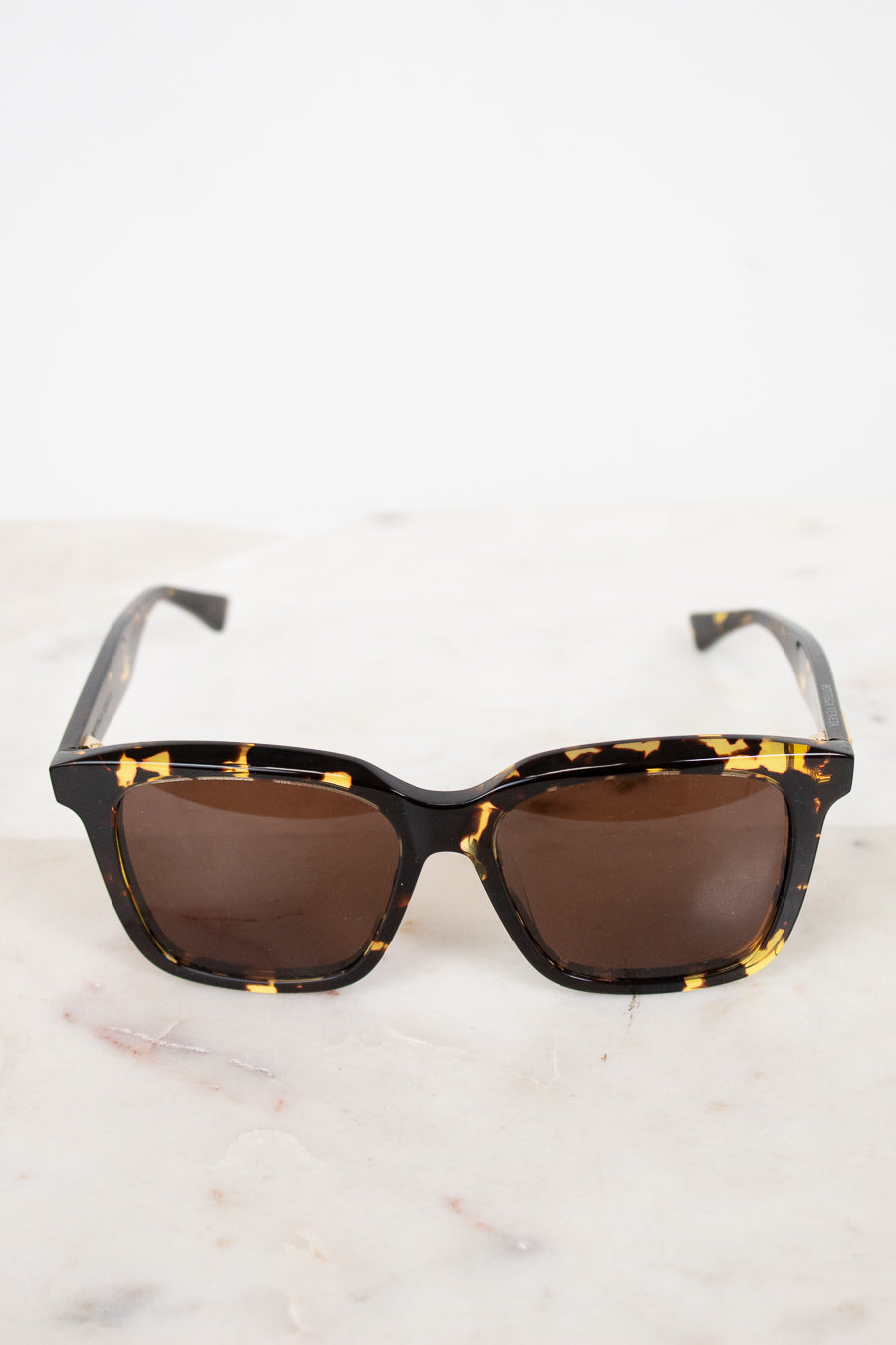Sunglasses with tortoiseshell frame and brown lenses on a light background