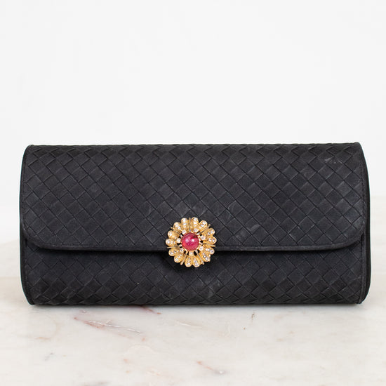 Black quilted clutch bag with a decorative clasp on a marble surface