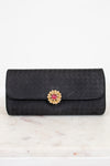 Black quilted clutch bag with a decorative clasp on a marble surface