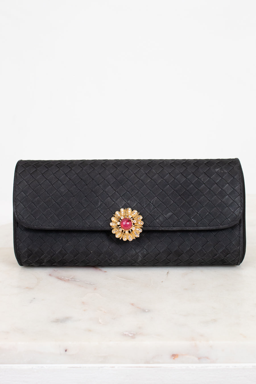 Black quilted clutch bag with a decorative clasp on a marble surface
