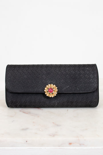Black quilted clutch bag with a decorative clasp on a marble surface