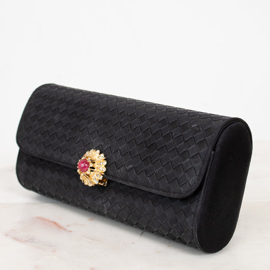 Black woven clutch with a decorative brooch on a marble surface