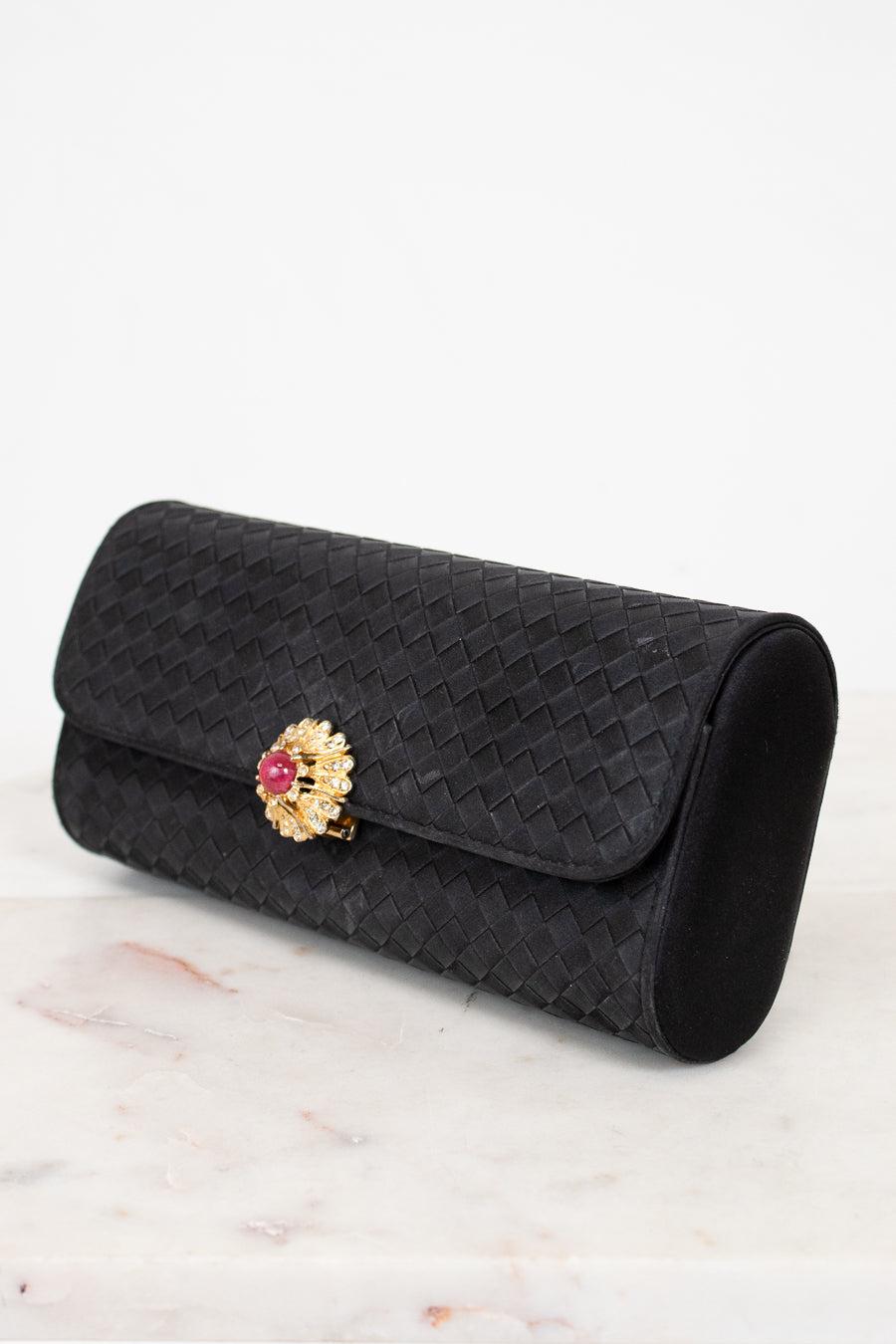 Black woven clutch with a decorative brooch on a marble surface