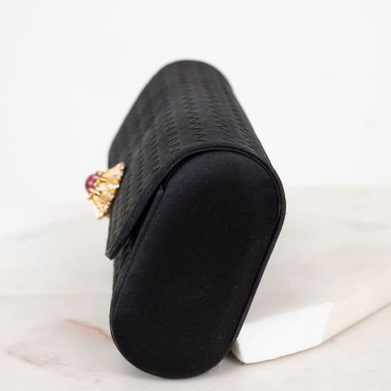Black clutch with a decorative brooch on a light marble surface