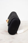 Black clutch with a decorative brooch on a light marble surface