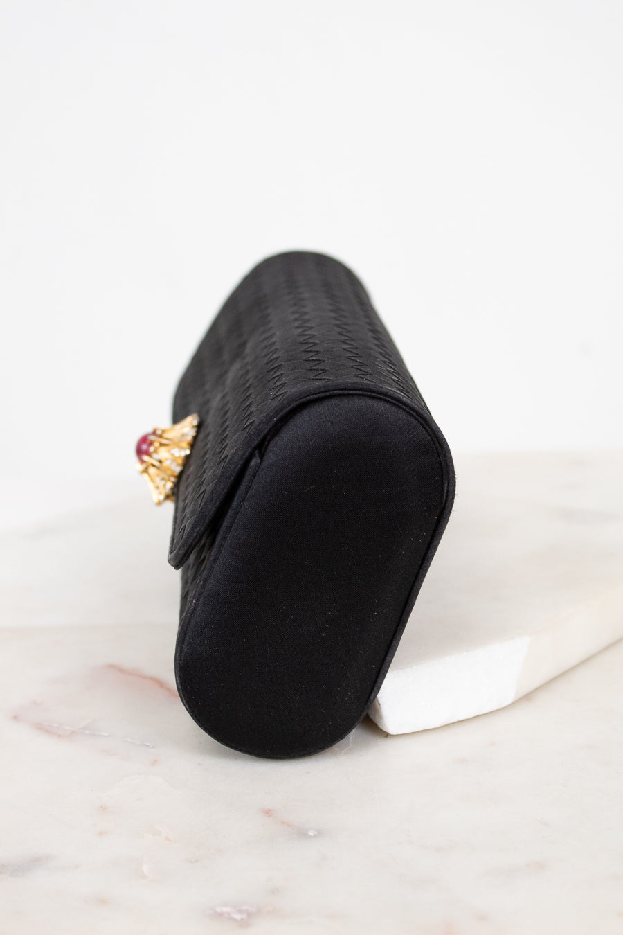 Black clutch with a decorative brooch on a light marble surface