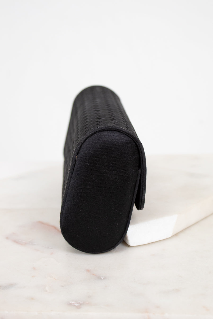 Black rectangular woven clutch on a light marble surface