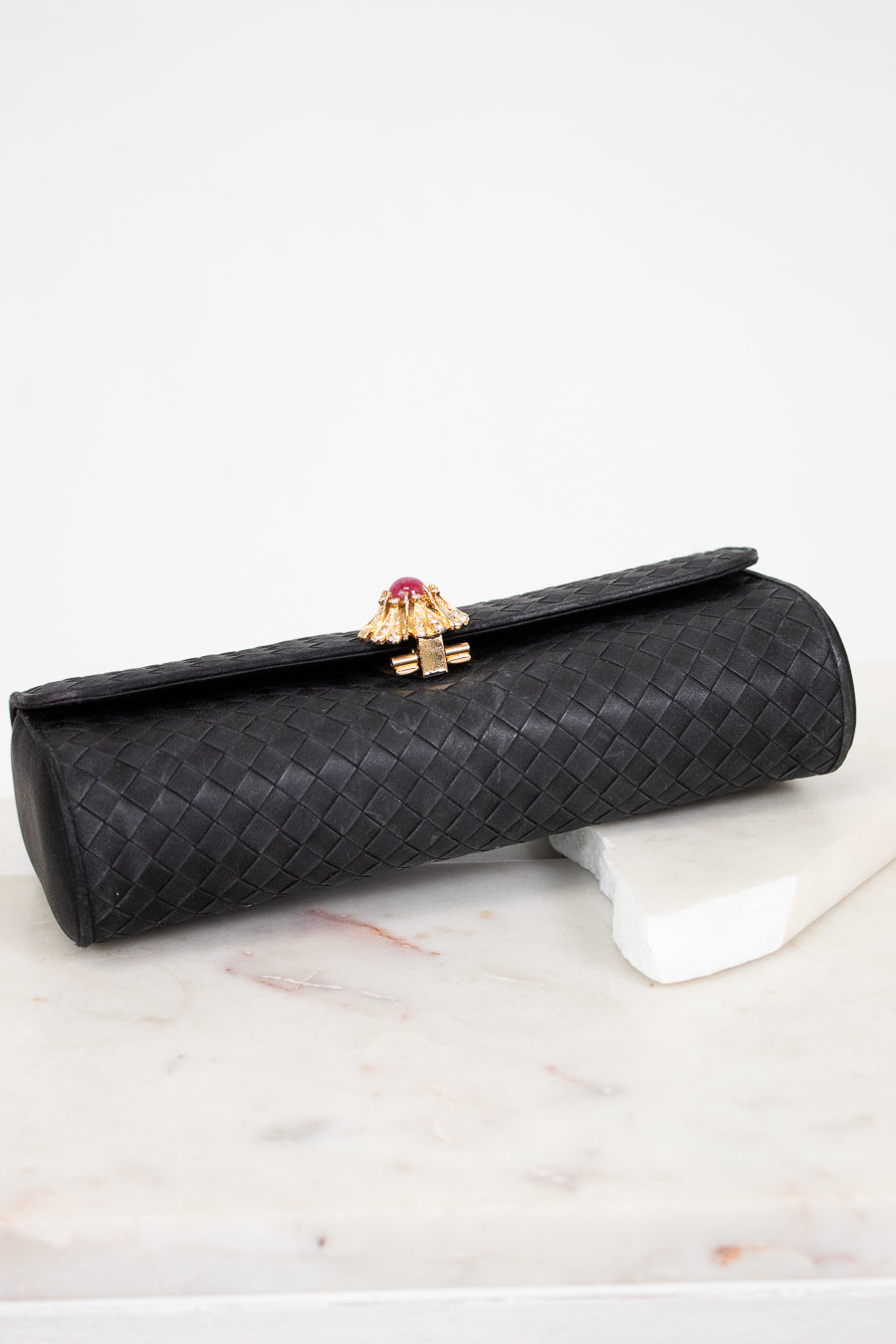 Black clutch bag with a gold clasp on a marble surface