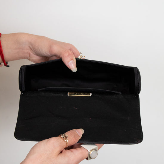 Black clutch held by a hand against a white background