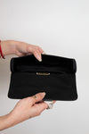Black clutch held by a hand against a white background