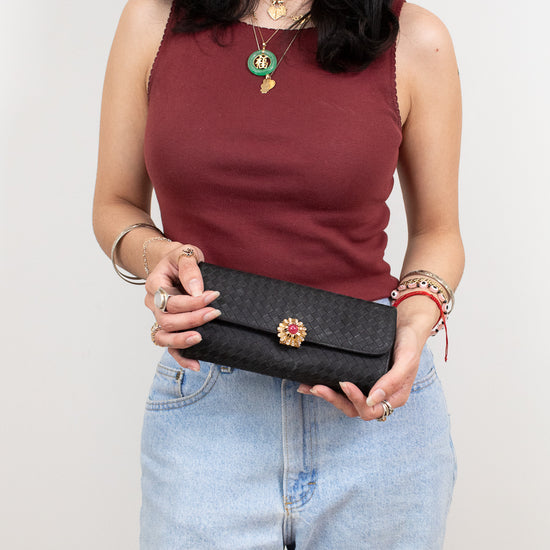 Woman holding a black clutch with a decorative element against a plain background