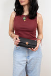Woman holding a black clutch with a decorative element against a plain background
