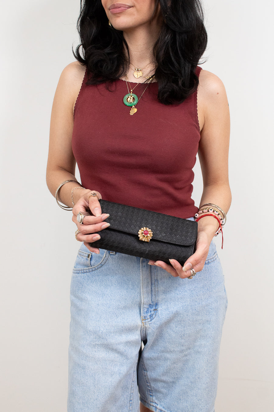 Woman holding a black clutch with a decorative element against a plain background