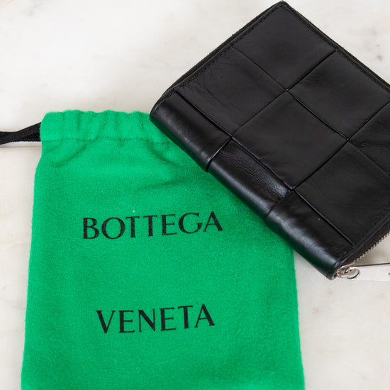 Black woven wallet with Bottega Veneta logo and green drawstring pouch on a light marble background