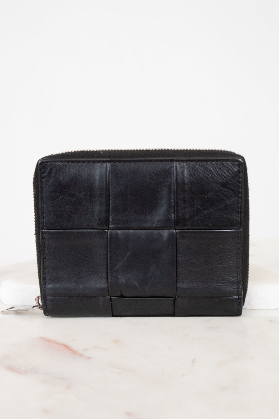 Black quilted wallet on a white marble surface