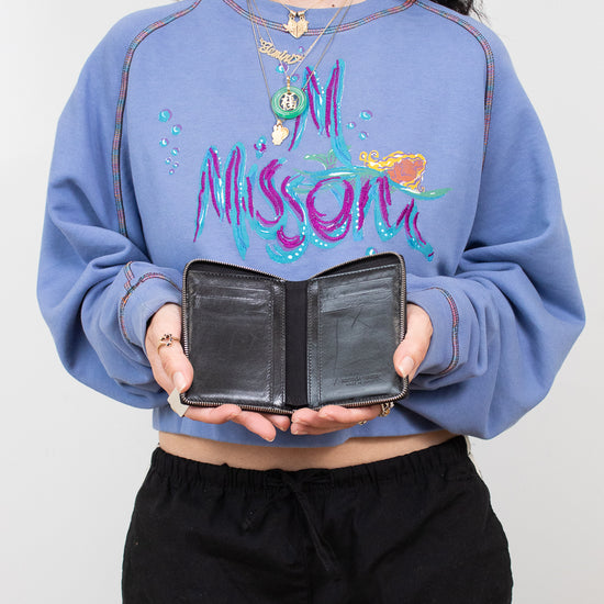 Person wearing a blue sweatshirt with colorful text, holding a black wallet against a plain background