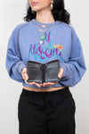Person wearing a blue sweatshirt with colorful text, holding a black wallet against a plain background