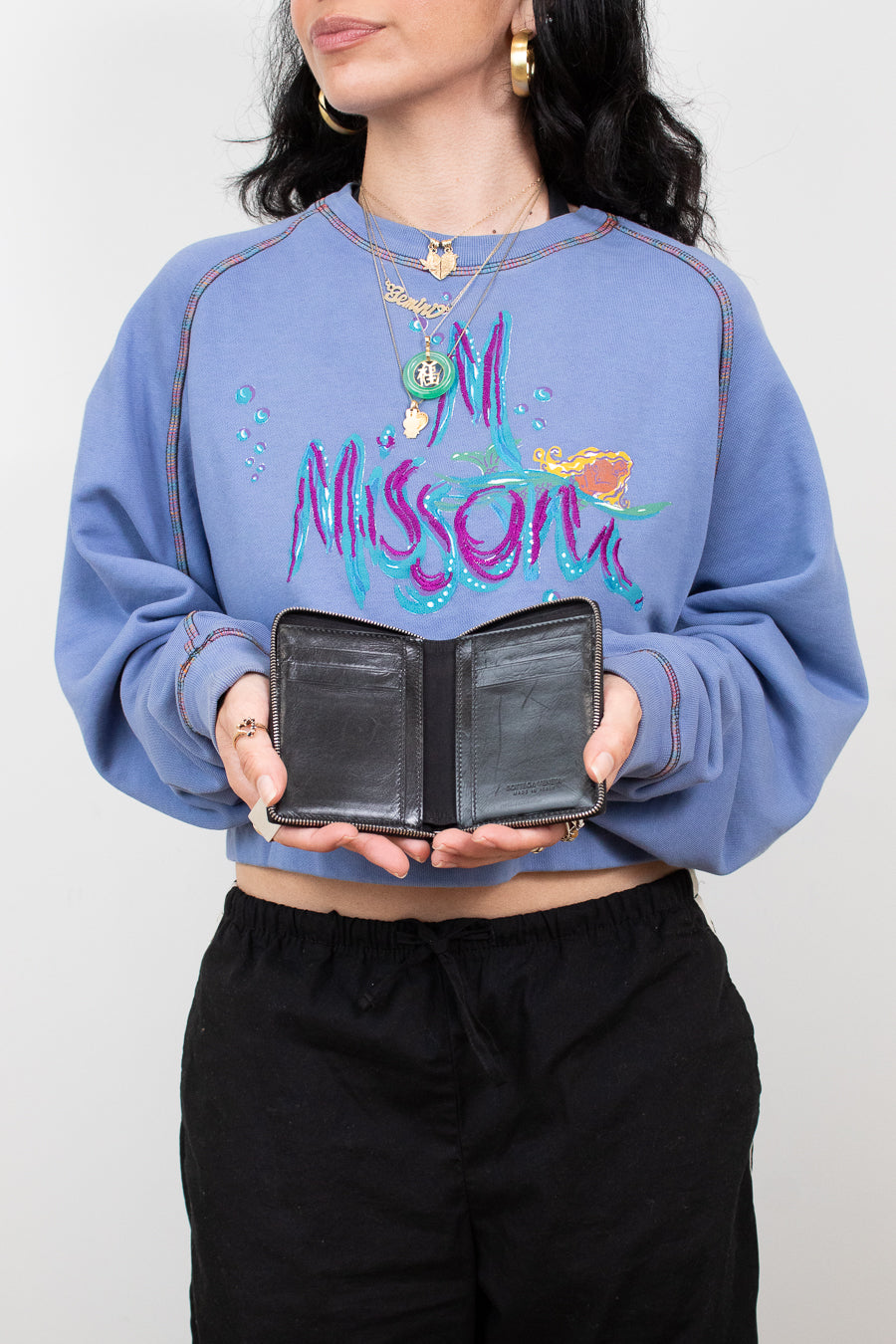 Person wearing a blue sweatshirt with colorful text, holding a black wallet against a plain background
