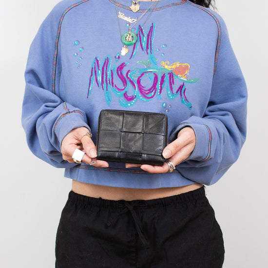 Person wearing a blue sweatshirt , holding a black wallet against a plain background